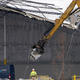 Workers use equipment to remove a section of roof left on a heavily damaged Amazon fulfillment center in Edwardsville, Illinois. An Amazon Prime delivery van sits in the lower left corner.